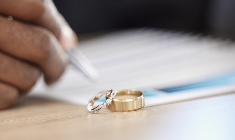 person signing divorce papers with rings in the foreground