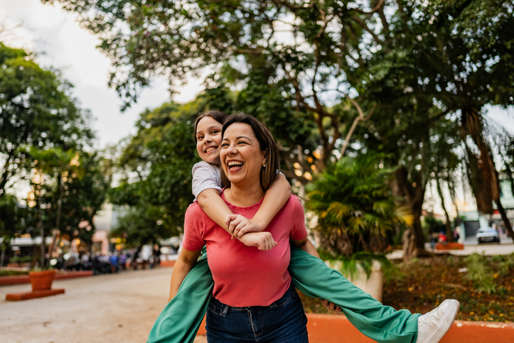 mother carrying daughter piggyback style in a park